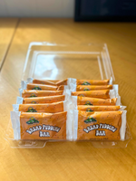 Packaged muffin town bread pudding bars in a clear plastic container on a wooden surface.